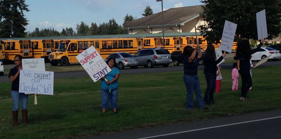Picketers hold signs in a field in front of school buses