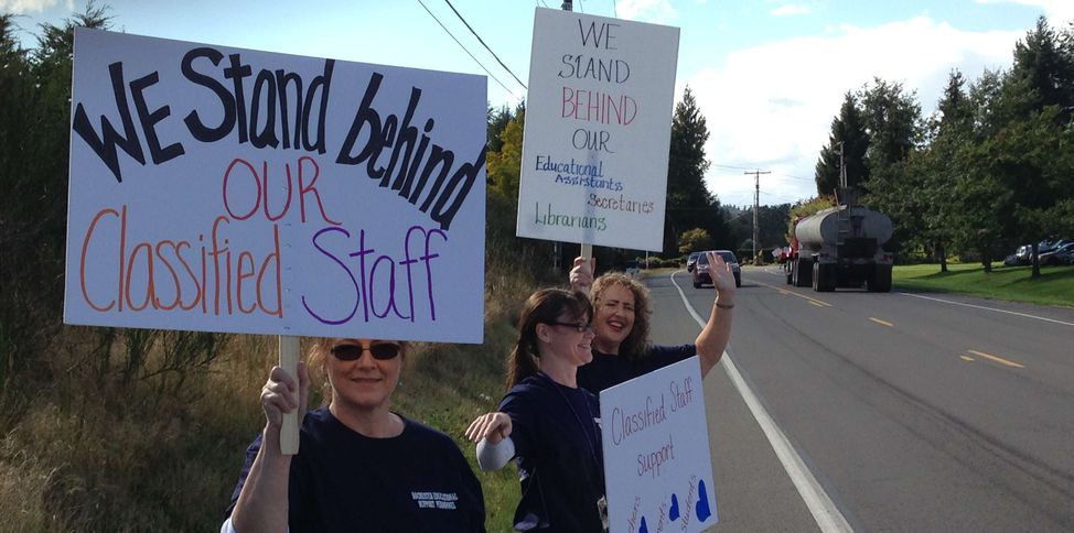 A picketter holds a sign reading "We stand behind our classified staff"